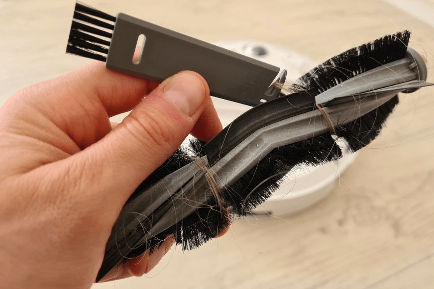 Haare werden aus der Hauptbürste des ECOVACS DEEBOT T10 mit Hilfe des beigefügten Reinigungswerkzeugs entfernt.